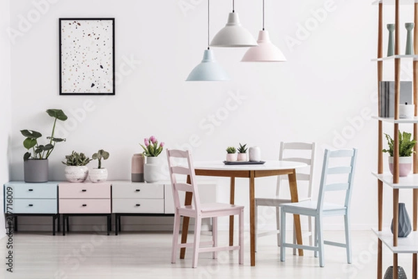 Fototapeta Real photo of a pastel dining room interior with a table, chairs, cabinets and poster