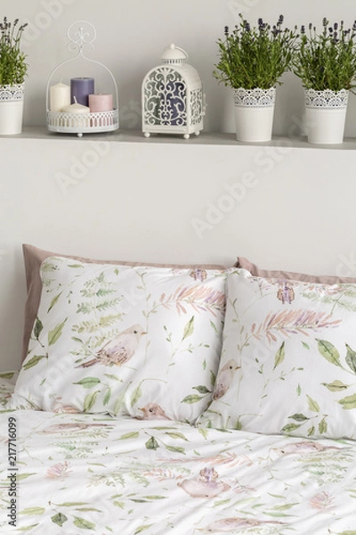 Fototapeta Real photo of wall shelf with fresh lavender, candles and decor above double bed with floral sheets