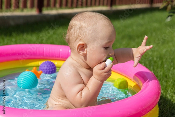 Fototapeta A small child is bathing in a pool, inflatable children's inflatable pool in summer	