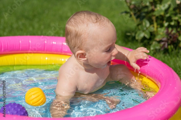 Fototapeta A small child is bathing in a pool, inflatable children's inflatable pool in summer	