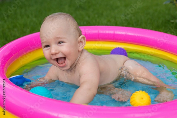 Fototapeta A small child is bathing in a pool, inflatable children's inflatable pool in summer	