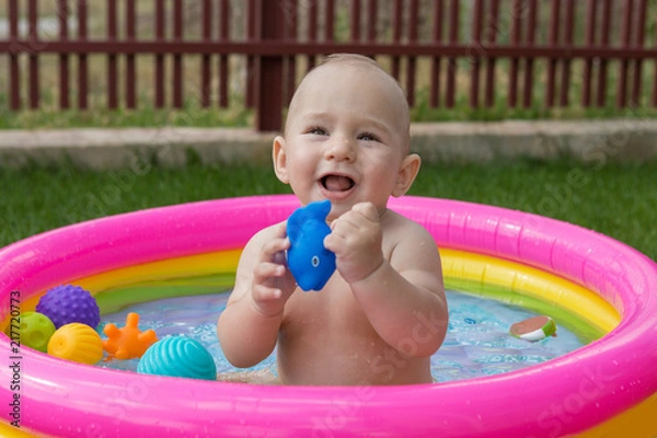Fototapeta A small child is bathing in a pool, inflatable children's inflatable pool in summer