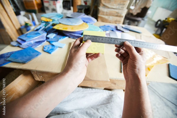 Obraz Master of mosaic measuring square pattern with ruler over workplace while choosing tiles for new order