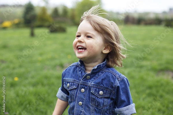 Fototapeta Outdoor portrait of a cute happy smiling young caucasian 1-2 years old toddler boy having fun running around in a park .