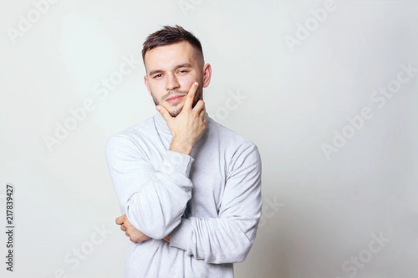Fototapeta Portrait of a handsome young man thinking on something, isolated on gray background