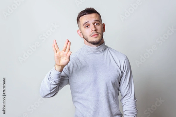 Fototapeta Geek saluting concept. Bristle men in white turtleneck shirt welcomes fans of fiction films Vulcan greeting on grey background copy space