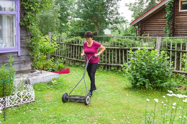 Obraz Garden work. Ederly woman mowing grass with lawn mower in the garden