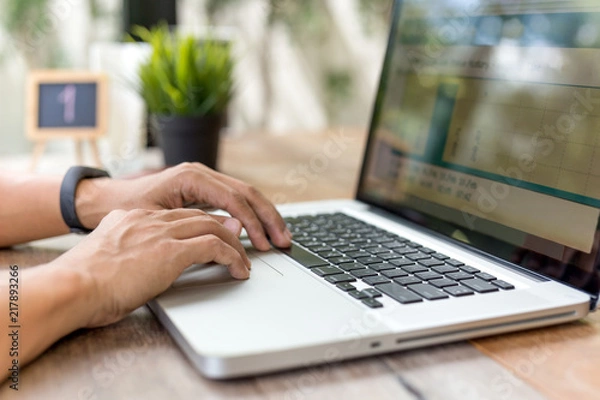 Fototapeta Businessman hands typing on laptop computer on wooden table in cafe.