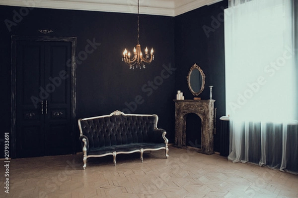 Fototapeta Black room in the castle with a window, a chandelier, a sofa and mirror and fireplace. Space where you can put a person.