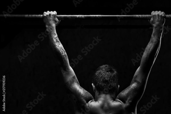 Fototapeta Strong young man doing pull up exercise on horizontal bar in gym. Sports, fitness, gymnastics workout.