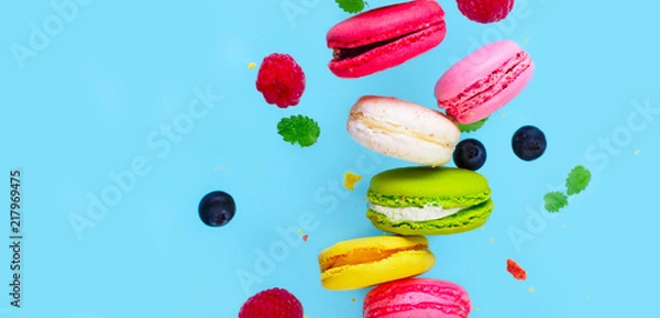 Fototapeta Assorted macaroons falling cookies with berries close up on blue background banner