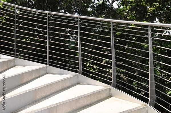 Fototapeta Spiral steps with stainless steel railings against a lush background of greenery
