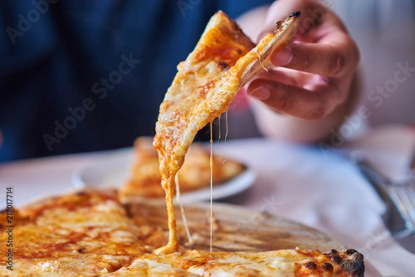 Fototapeta Close up a hot pizza slice with dripping mozzarella cheese.