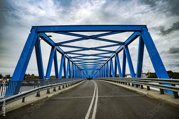 Fototapeta Blue metal bridge with clouds in the background.