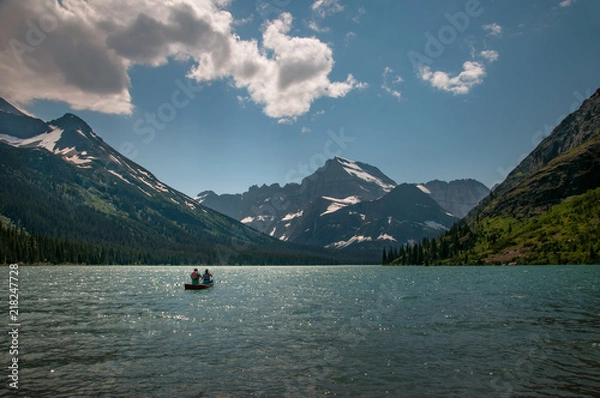 Fototapeta Couple canoeing on lake with snowy mountains, blue sky and clouds