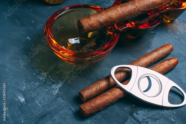 Fototapeta scotch whisky in old fashion glass and decanter with smoking cigar in ashtray on gray concrete background