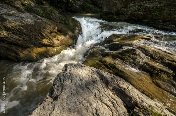 Fototapeta Wide angle shot of mountain river with a waterfall flowing between rocky coasts. Expressive foreground. Taken from low point of view at sunny spring day at Carpathian mountains. Natural background. 