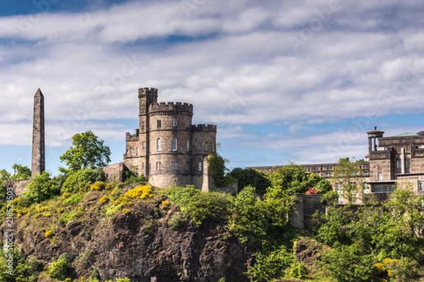 Fototapeta Edinburgh, Scotland, UK - June 13, 2012: Martyrs of reform Monument and Governor House of Old Calton Jail on green cliff under cloudy sky.