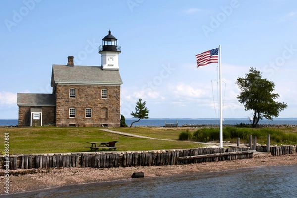 Obraz American Flag Flying Near Stone Lighthouse in Connecticut