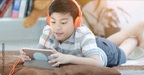 Obraz Asian boy lying and Playing Game On Digital Tablet At Home