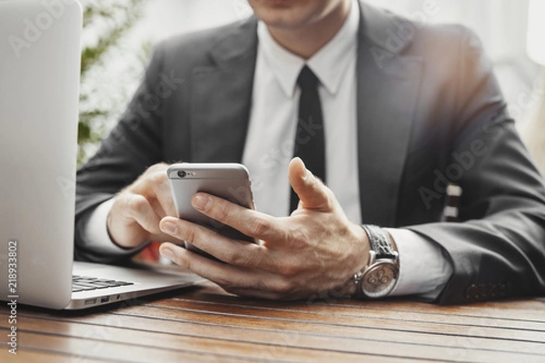 Fototapeta Close up of businessman looking at mobile phone and working with laptop.
