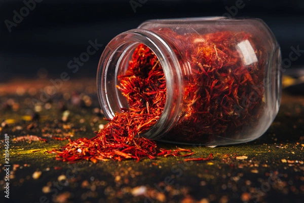 Fototapeta Saffron spice in an open glass jar on dark black background. Seasonings for food. Close-up.