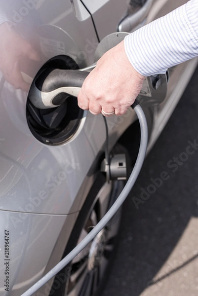 Obraz Frau lädt ihr Elektrofahrzeug mit einem Ladekabel