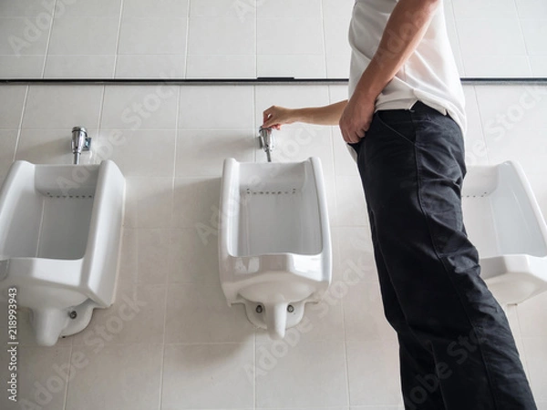 Obraz Man standing press flushing a urinal in a public washroom
