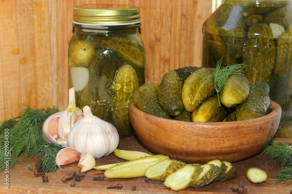 Fototapeta Cucumbers in a wooden bowl, fresh herbs, pickling spices and jars of pickled cucumbers on the table