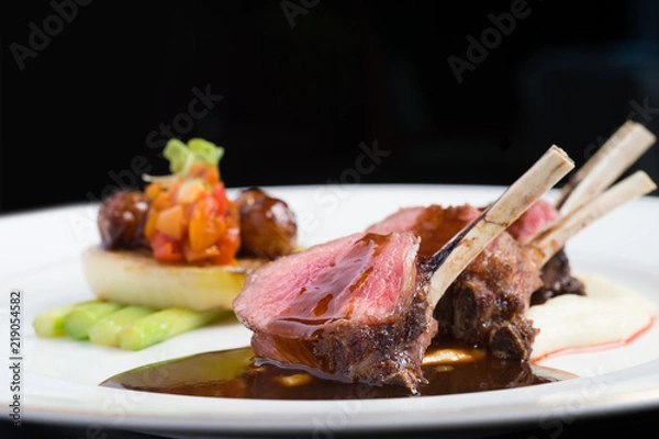 Fototapeta close up lamp rack pored by stocks with asparagus and sliced tomato, cucumber, onion, apricot, carrot on white plate lighted by studio light  