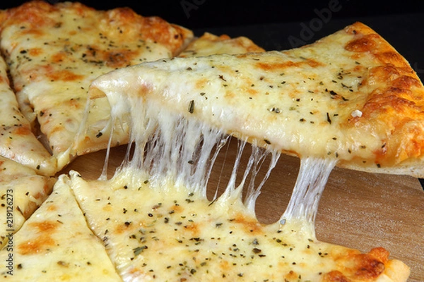 Fototapeta Hot appetizing cheese pizza, cut into pieces, one of which is picked up