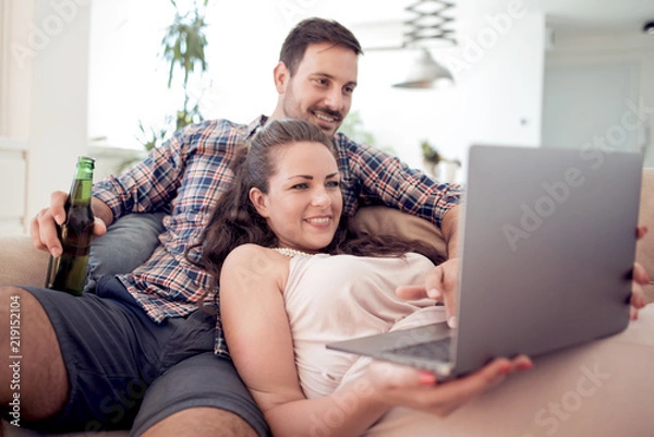 Obraz Couple sitting on sofa and using laptop in living room
