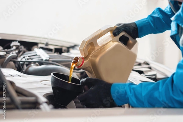 Obraz The auto mechanic pours new clean engine oil through the funnel. replacement of engine oil in the machine. car service worker