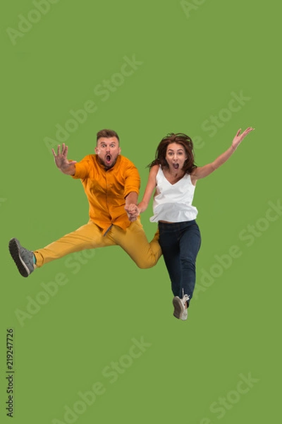 Obraz Freedom in moving. Pretty young couple jumping against green background