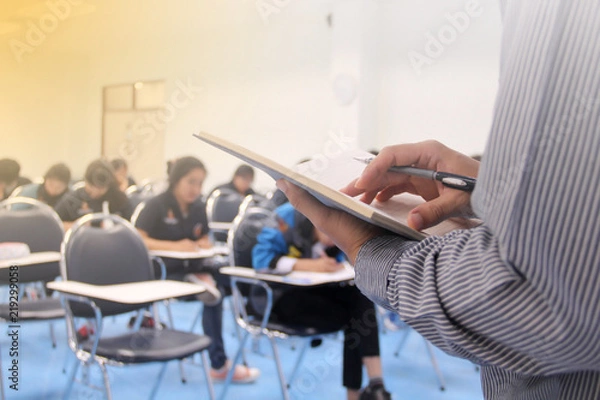 Fototapeta Teacher teach students and background of students during study or quiz, test and exams in large lecture room / University classroom. Students are in uniform classroom educational school.