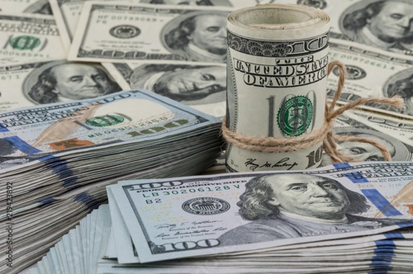 Fototapeta A roll of one hundred dollar bills tied with a rope against the backdrop of scattered dollars.