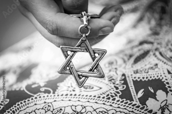 Fototapeta Young woman's hand holding a Star of David - Magen David key chain. The State of Israel, Holocaust remembrance, Judaism, Zionism concept image. Black and white image.