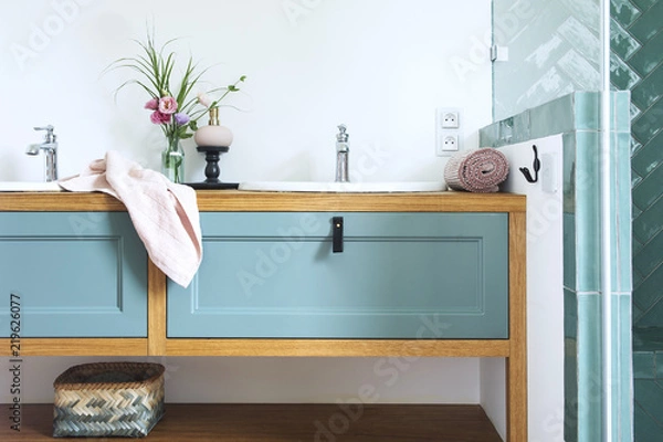 Fototapeta Bathroom sink with blue drawers, pink towel and bouquet