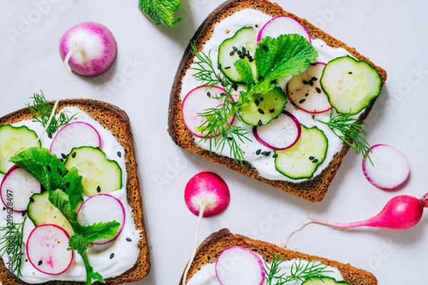 Fototapeta Toast with radish, cucumber and black sesame of dark bread on a light marble background