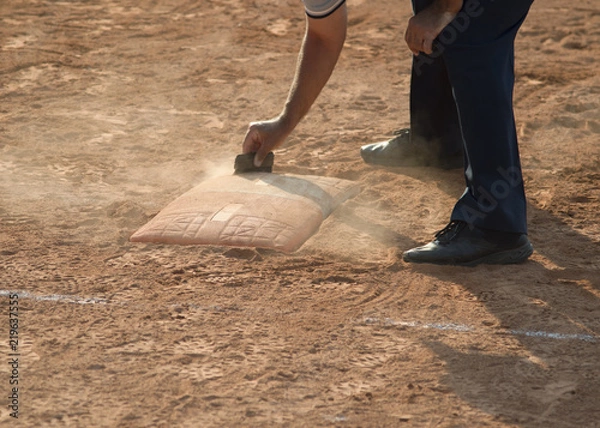Fototapeta Referee cleans home plate in a baseball (softball) dusty field, with copyspace