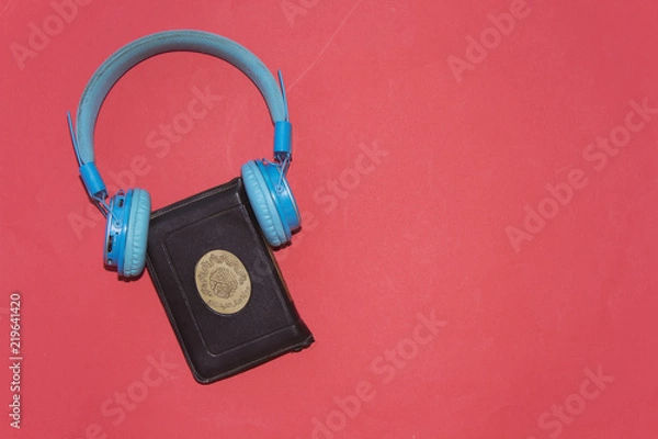 Fototapeta listen to quran concept, holy muslim book and bluetooth headphone  isolated on red background