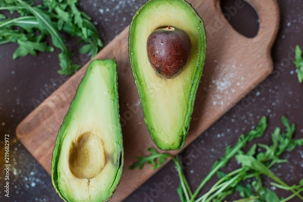Fototapeta Cut avocado, arugula and olive oil on a chopping board