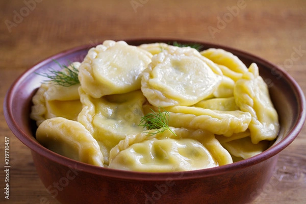 Fototapeta Dumplings, filled with cheese - vegetarian dish. Varenyky, vareniki, pierogi, pyrohy in a bowl on wooden table. horizontal