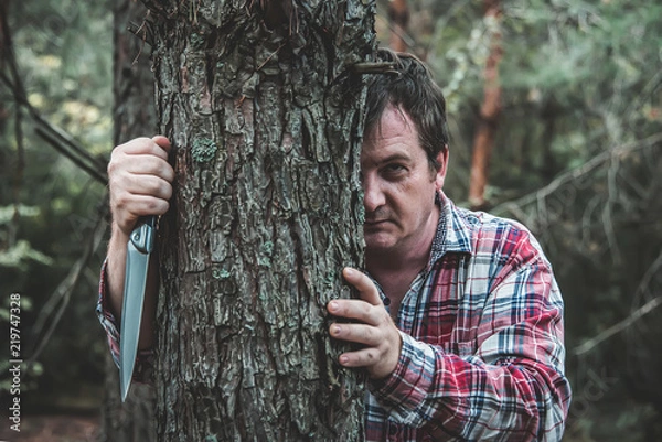 Obraz maniac with a knife stands behind a tree