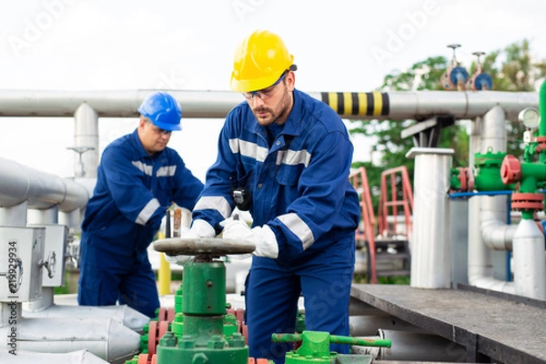 Fototapeta Two petrochemical workers inspecting pressure valves on a fuel tank