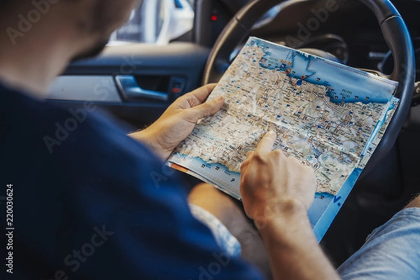 Fototapeta Close up of young man looking at map behind the wheel in car.