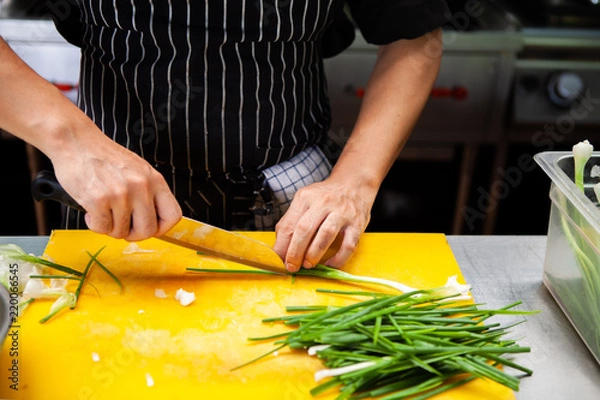 Fototapeta Professional Chef is using a kitchen knife to slice Scallions or Spring onion. Green onions may be cooked or used raw as a part of cooking around the world, especially Asian recipes. Natural lighting.