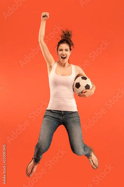Obraz Forward to the victory.The young woman as soccer football player jumping and kicking the ball at studio on a red background. Football fan and world championship concept. Human emotions concepts