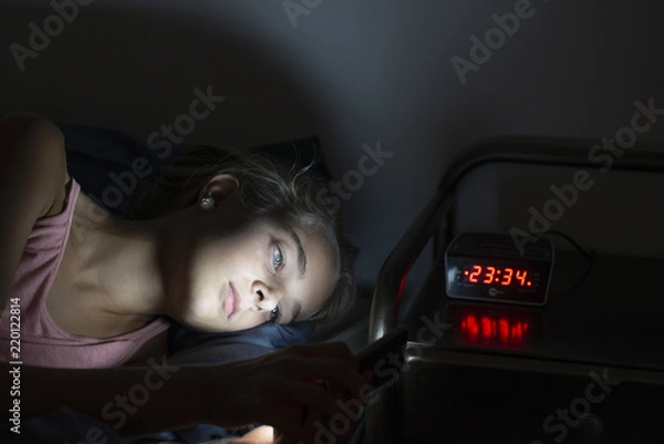 Fototapeta young girl using smartphone in bed at night. Mobile addiction.