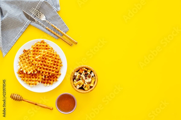 Fototapeta Hot round waffles ready to eat. Belgian recipe. Waffles on plate near honey and dried fruits on yellow background top view copy space